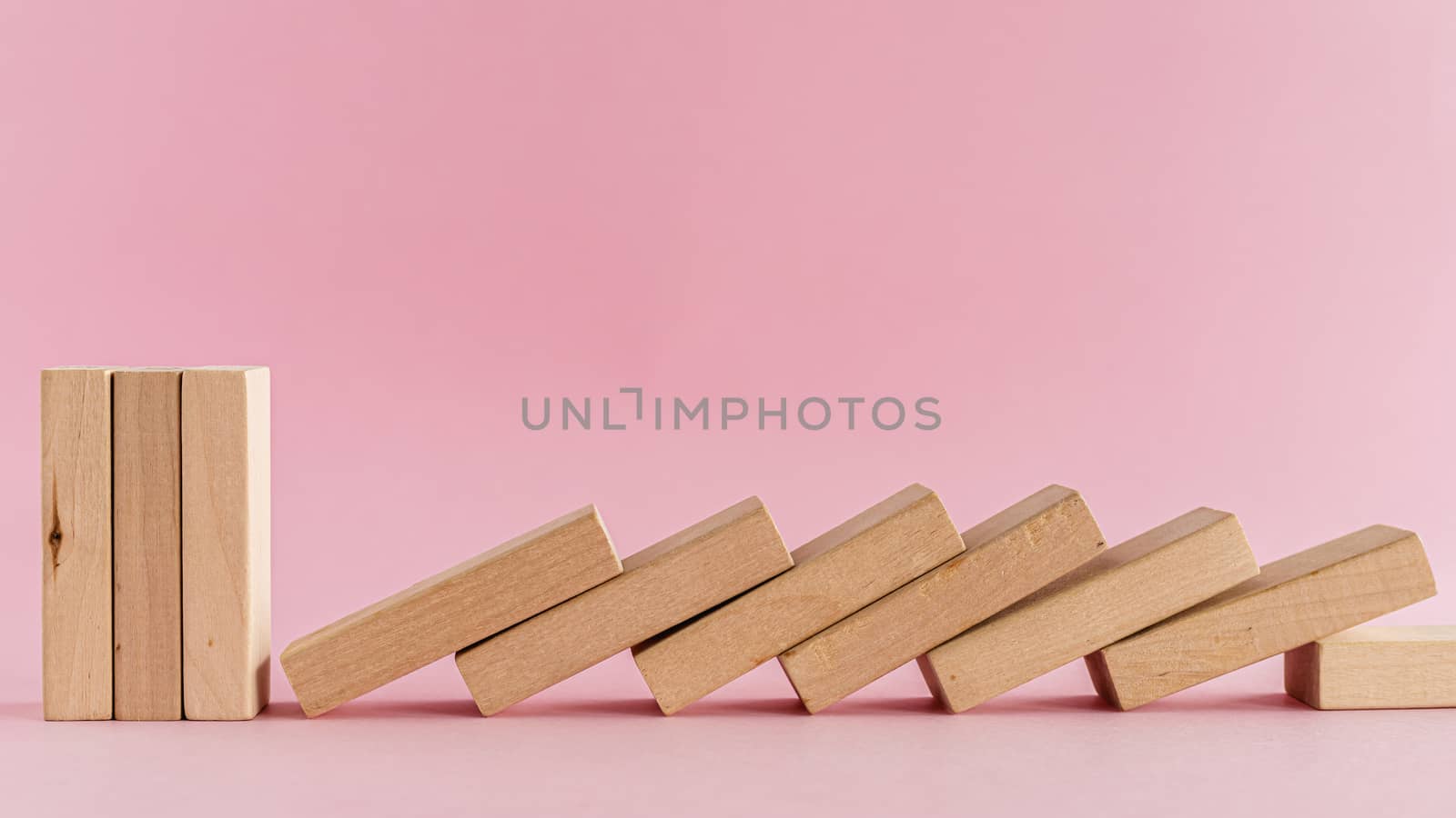 The wooden toys arranged in a horizontal row but the next others falling down on pink background for leisure activities concept