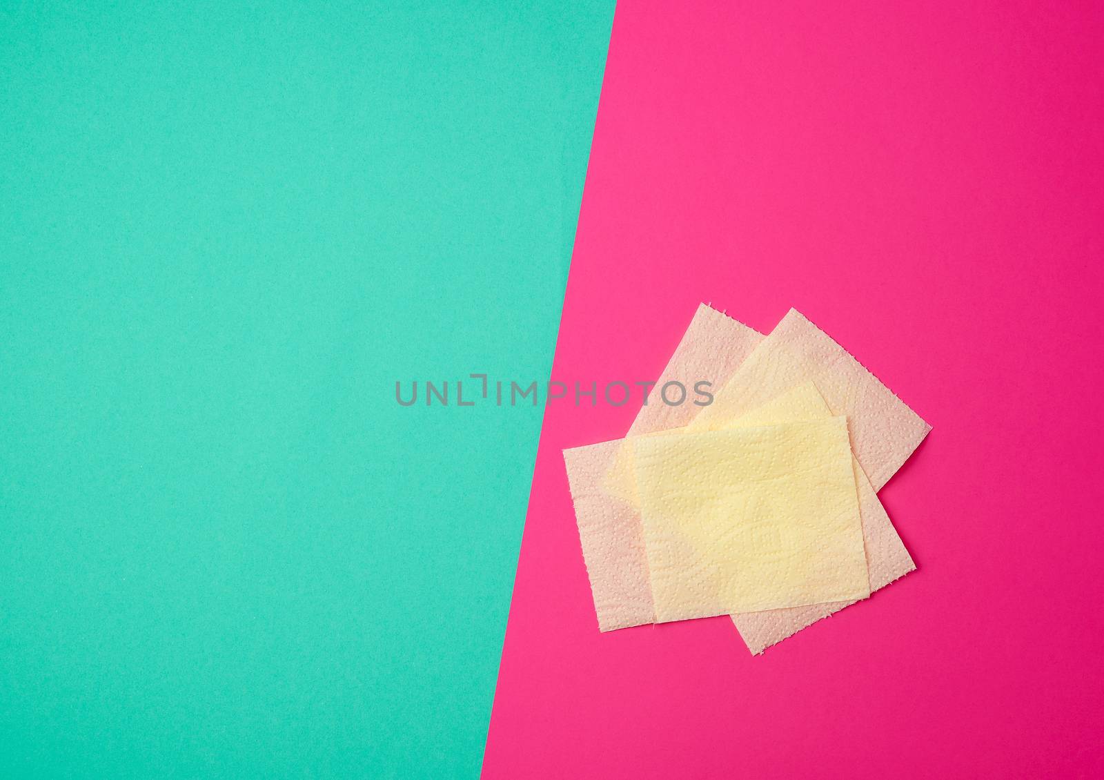 pieces of soft yellow toilet paper on a green-pink background, top view, copy space