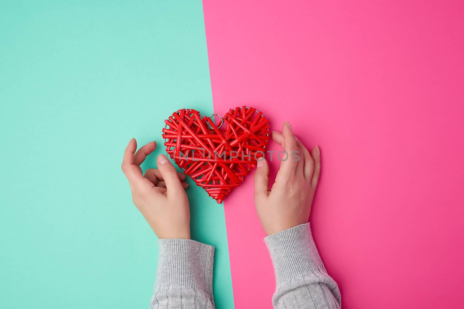 two female hands holding a red wicker heart a symbol of love on a green-pink background, top view