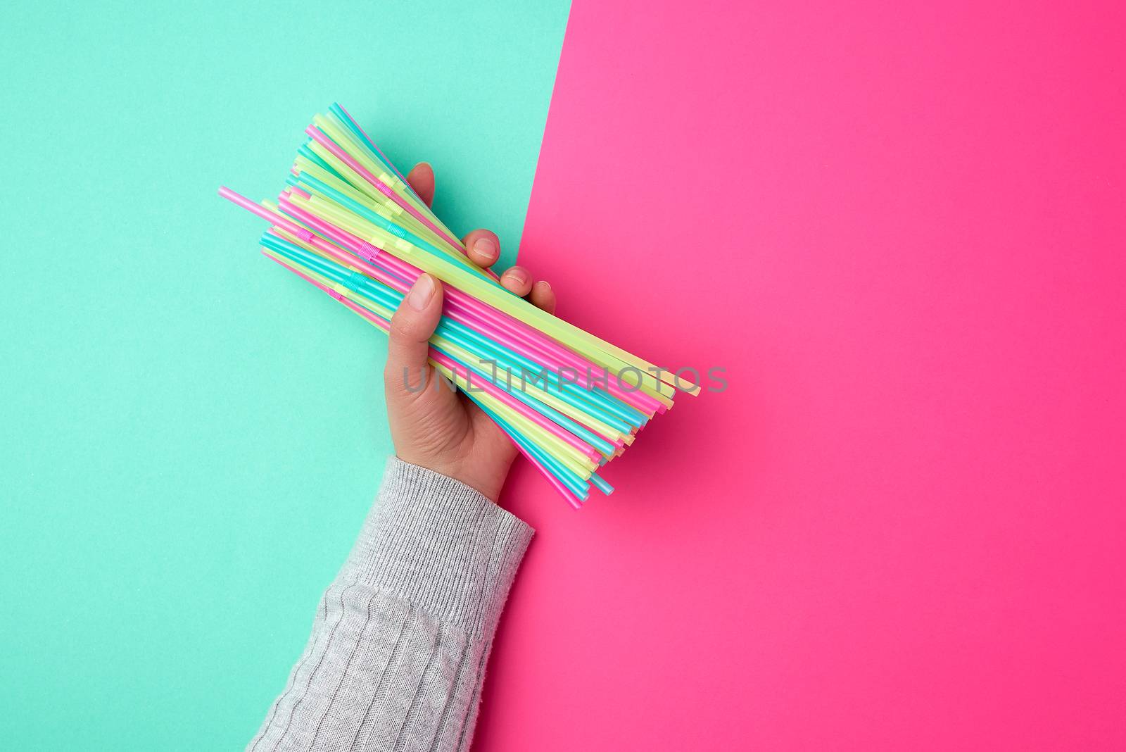 female hand holding multicolored plastic cocktail tubes, green pink background