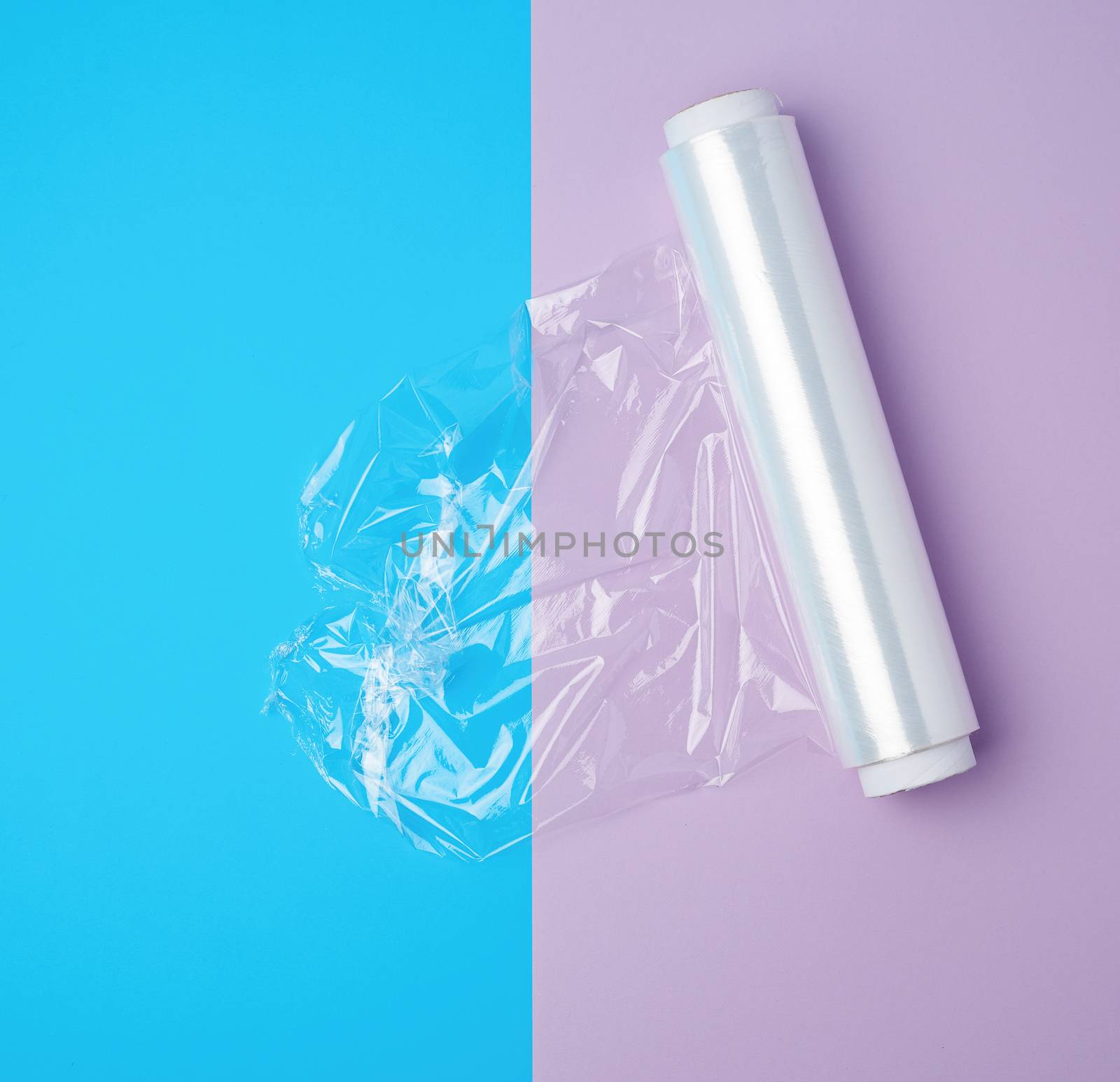 roll with transparent white polyethylene for wrapping products and packaging goods on a colored background, top view