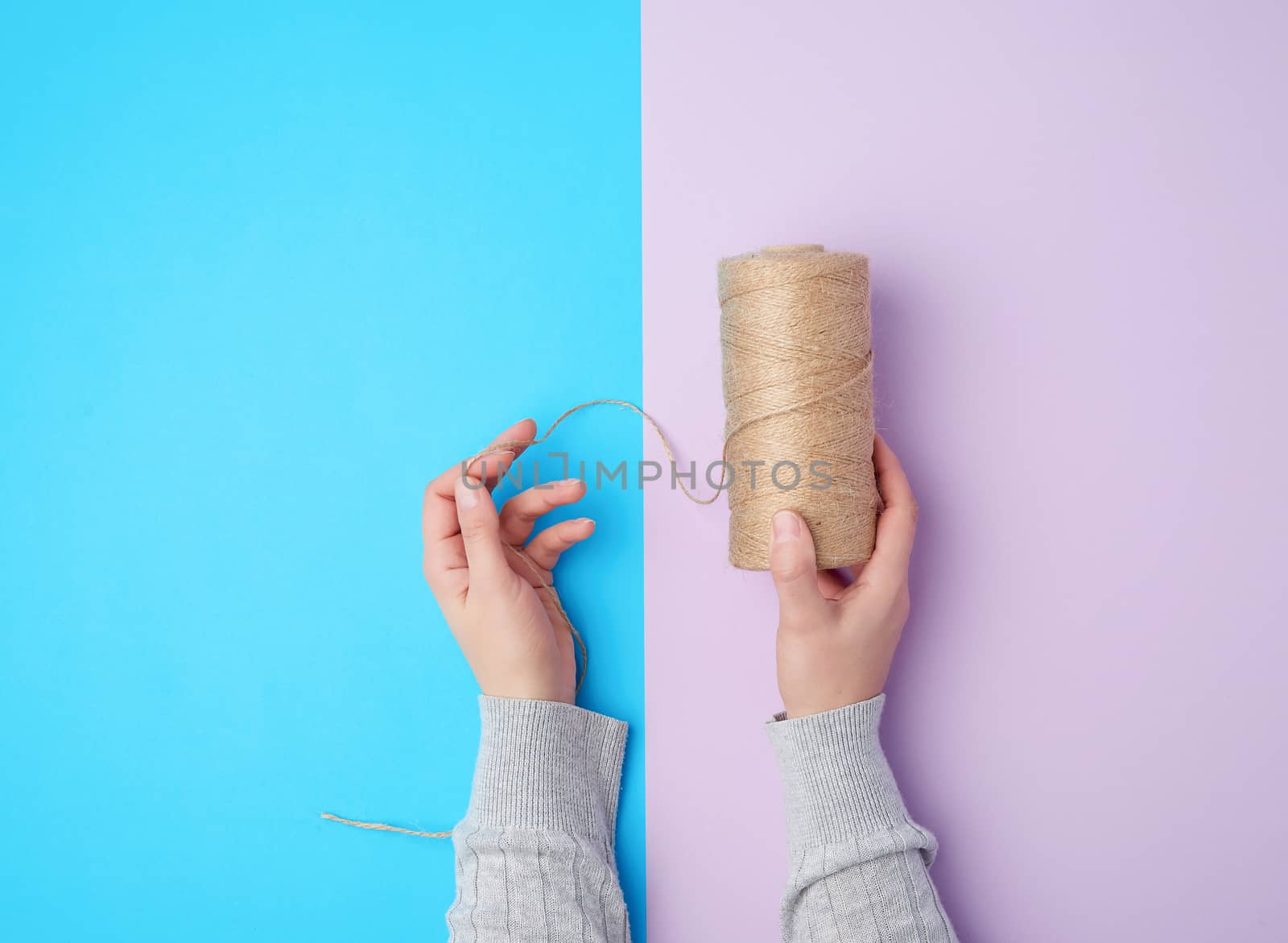female hands holding a skein with brown eco thread on a colorful background, top view