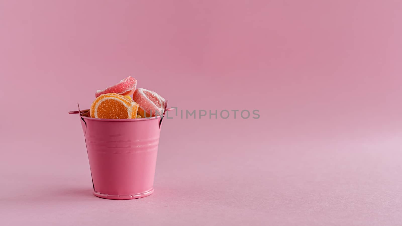 Full of colourful fruit Jelly candy in a pink bucket against pink background for food and snack concept