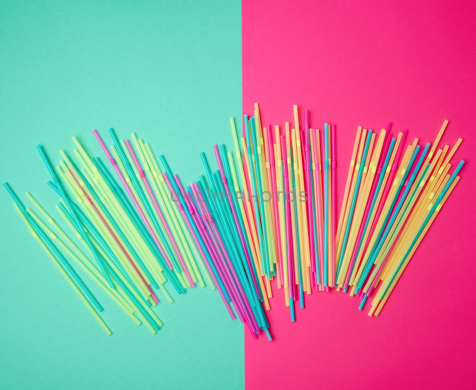 stack of multi-colored plastic tubes for a cocktail on a multi-colored background,  concept of environmental pollution by objects that decay in the ground for a long time, top view