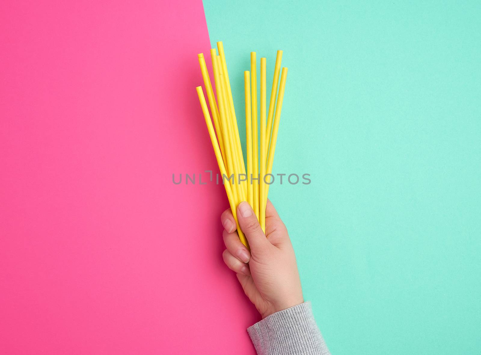 hand holds a stack of yellow paper tubes for a cocktail on a multi-colored background, concept of rejection of plastic and the use of recyclable materials