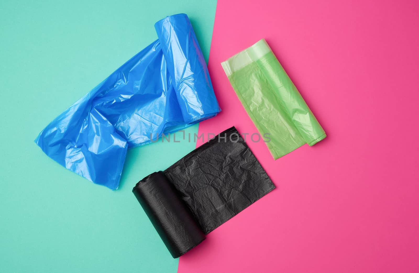 three rolled up rolls with plastic garbage bags on a green pink background, top view