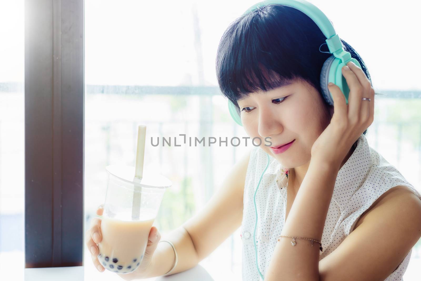 Asian woman wearing headphones and holding a plastic cup of bubble tea with blurred background for drinks, beverage and stay at home concept