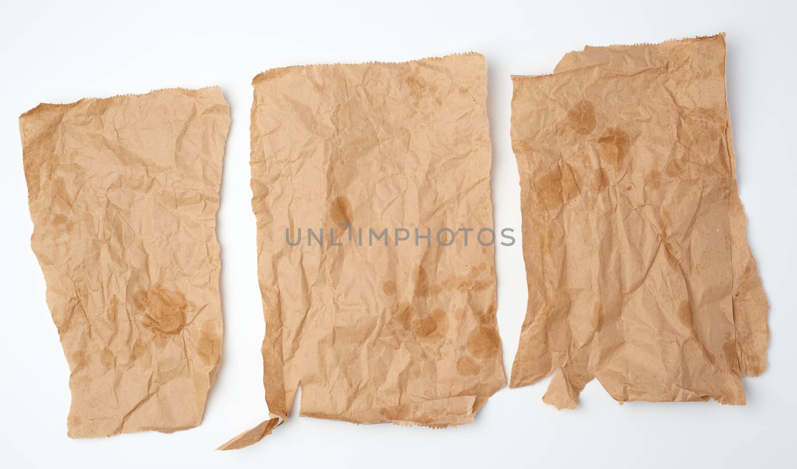 three torn crumpled pieces of brown paper with grease stains on a white background, top view
