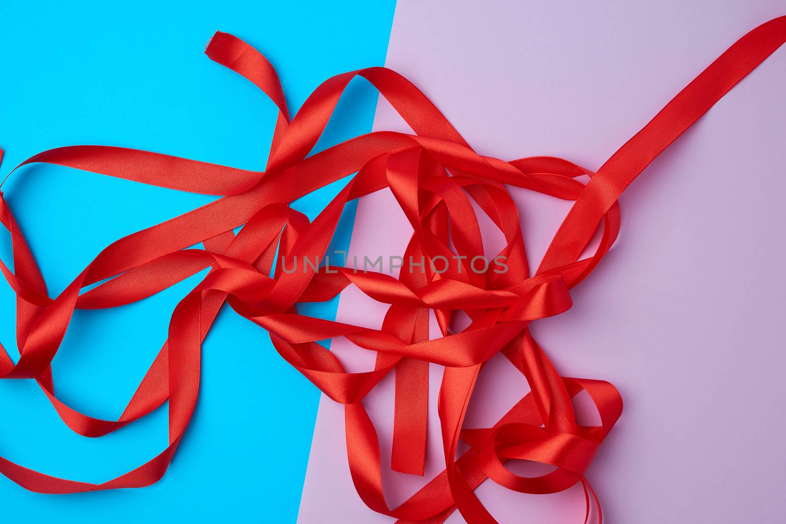 lot of red satin ribbon on a colored background, preparation for gift wrapping, top view