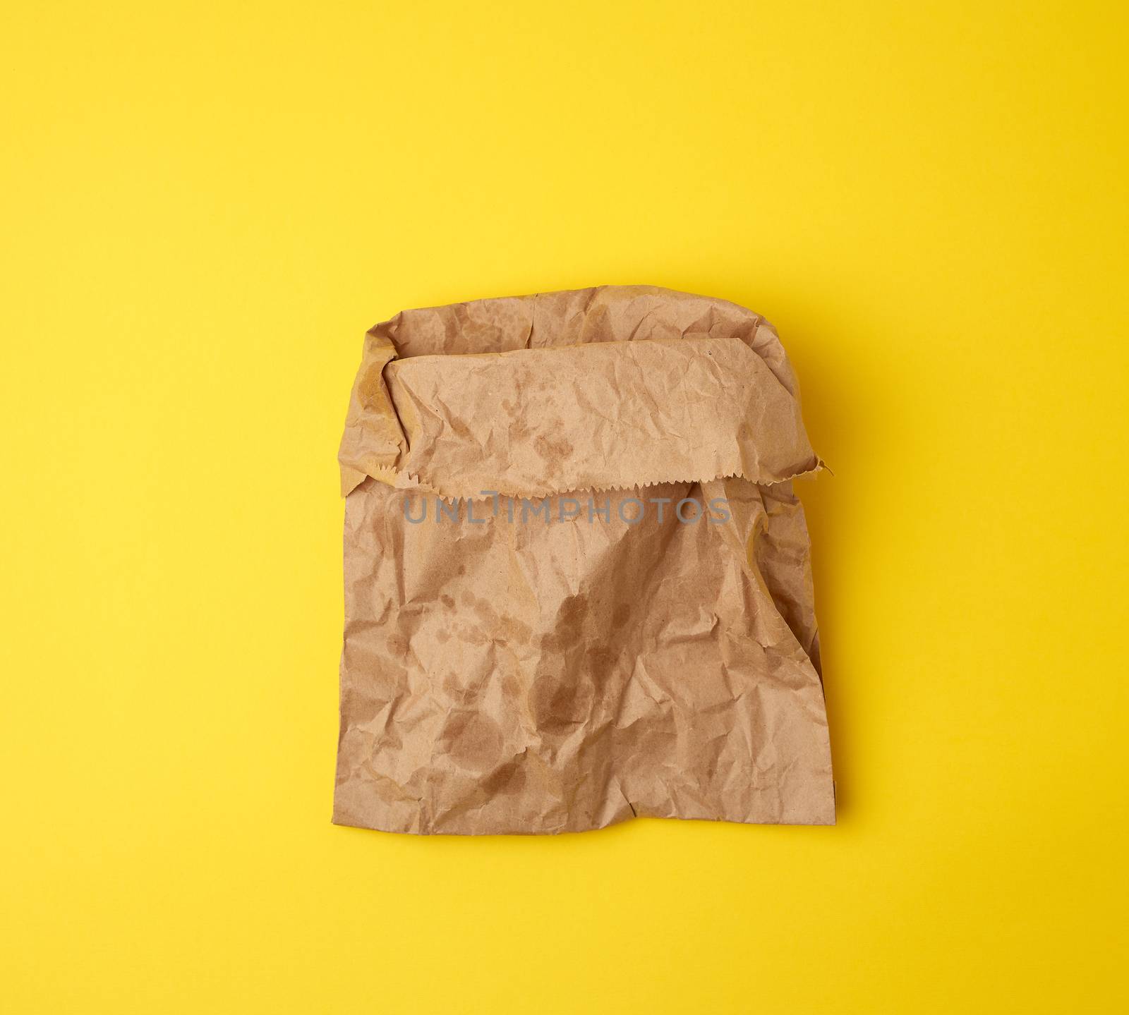 open brown paper bag for food packaging with greasy stains on a yellow background, concept of rejection of plastic bags to save the environment
