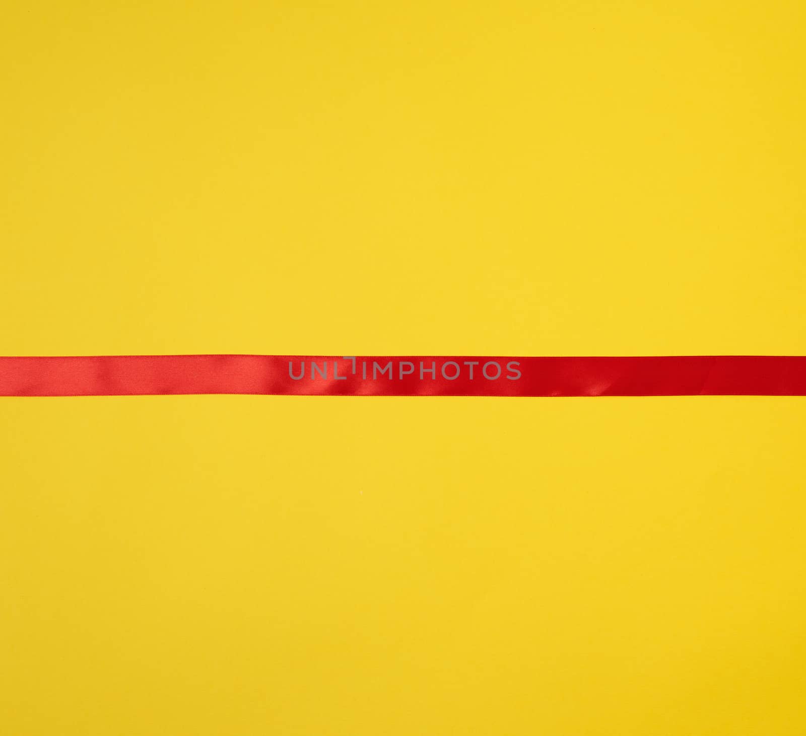 red silk ribbon on a yellow background, festive backdrop, place for text