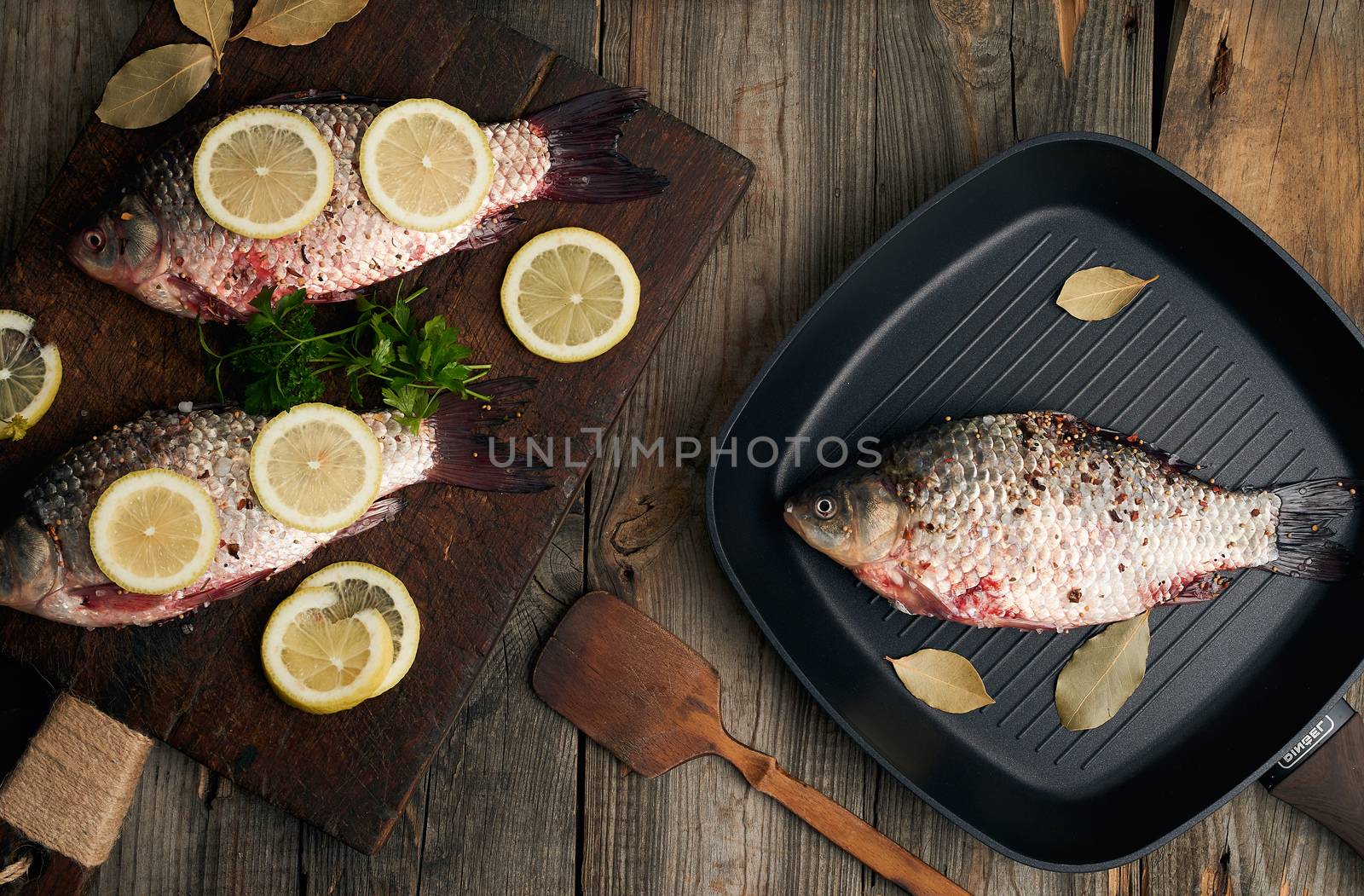 fresh fish in crucian scales on a brown old wooden cutting board, food seasoned with spices and slices of lemon, top view