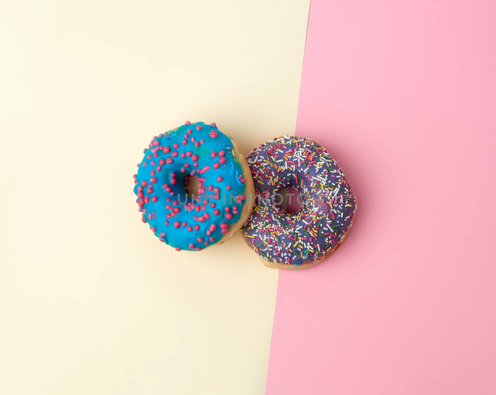 round baked donut with colored sugar sprinkles and with blue sugar glaze on a pink-yellow background, top view