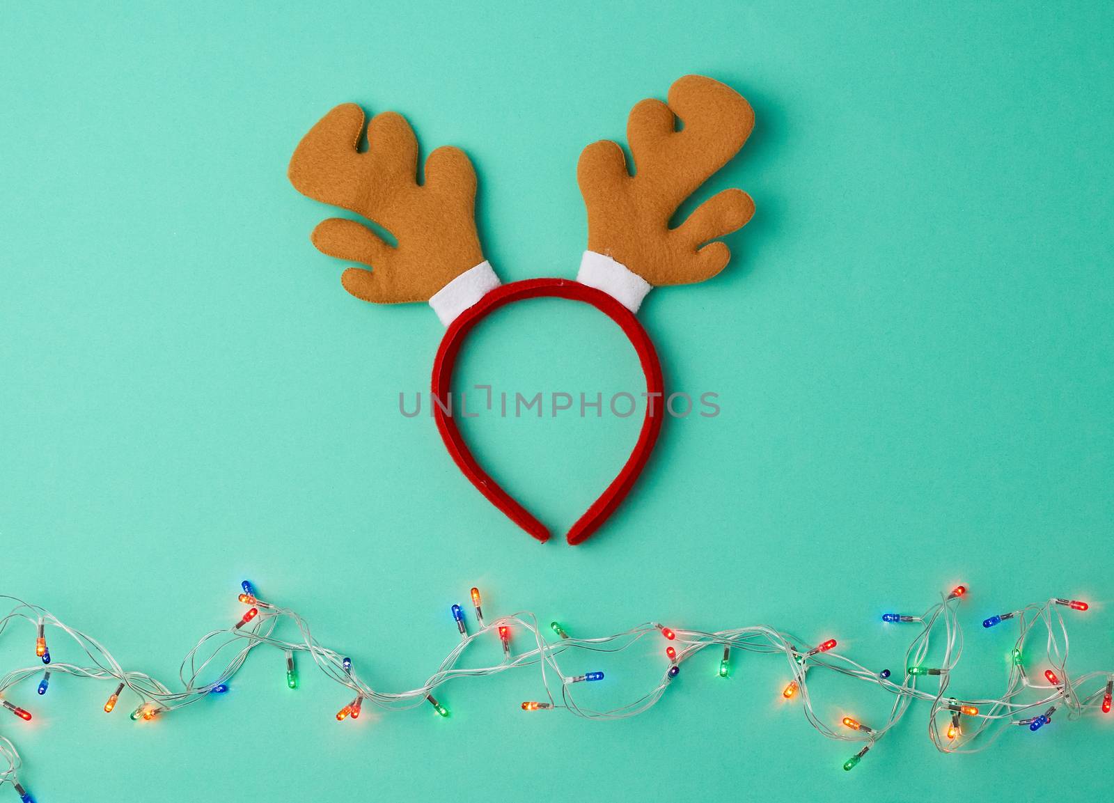 burning christmas garland on a white wire with colorful lights and carnival deer head mask on a green background, copy space
