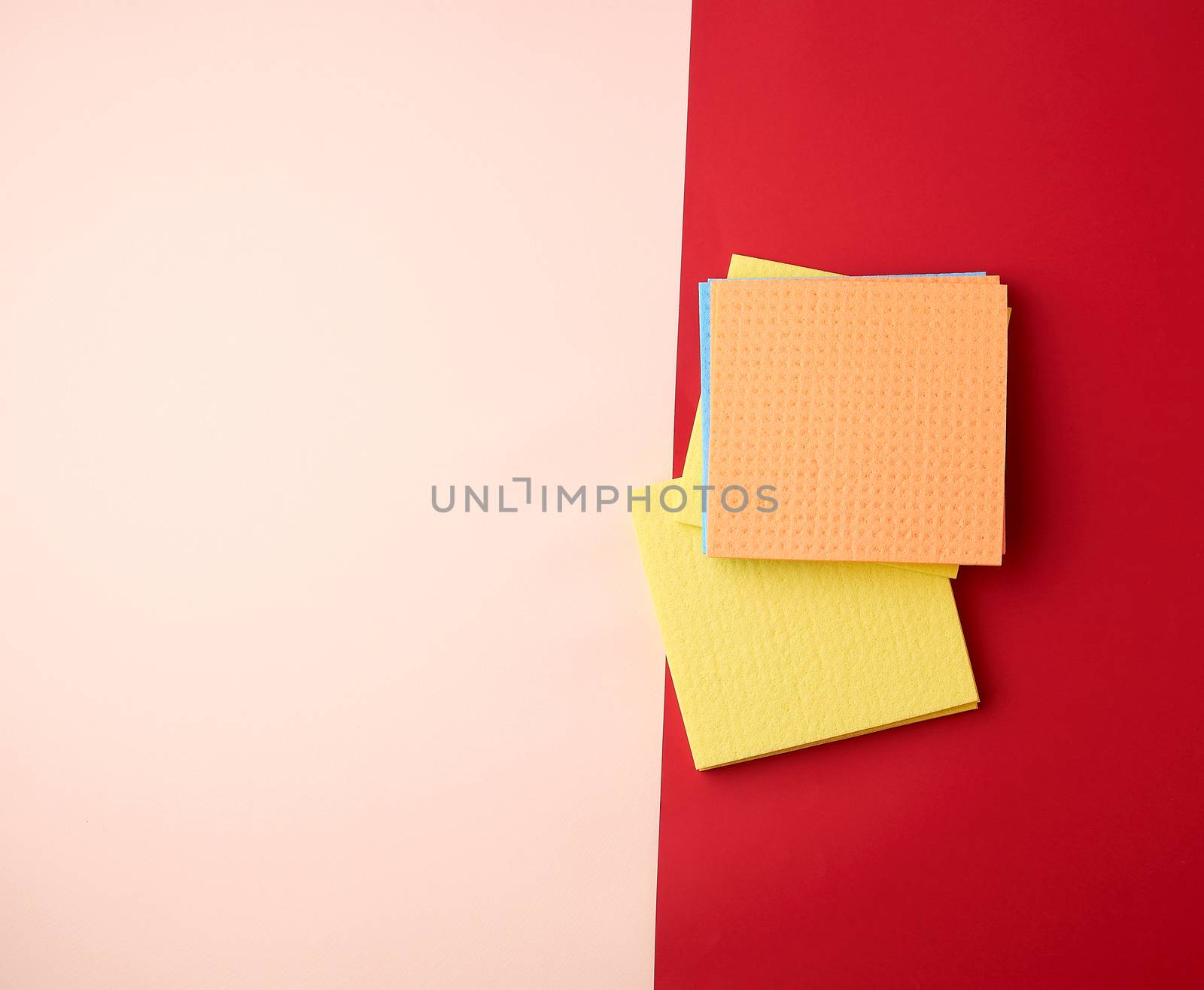 multi-colored square dishwashing sponges on a red-beige background, top view, flat lay