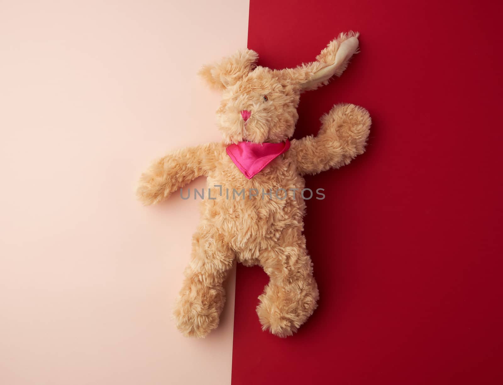 toy brown plush hare lies on a pink background, copy space