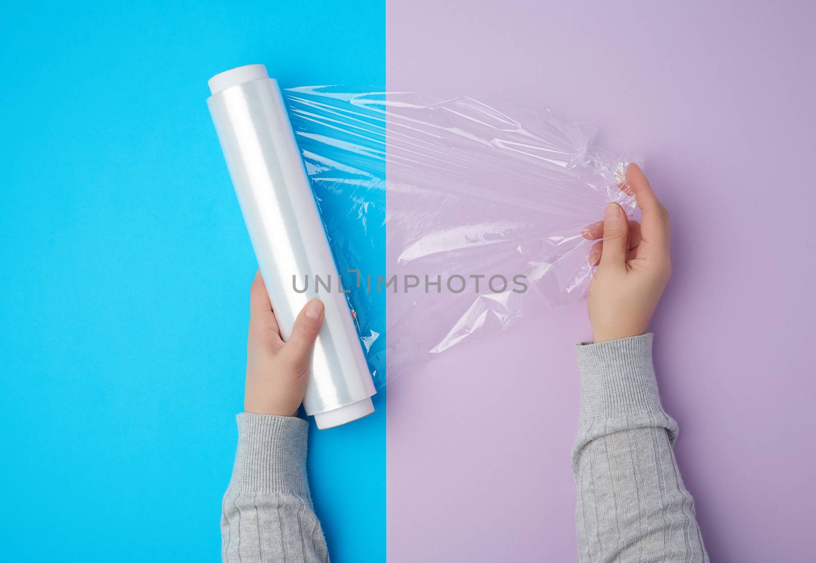 two hands hold a large roll of wound white transparent film for wrapping food, top view