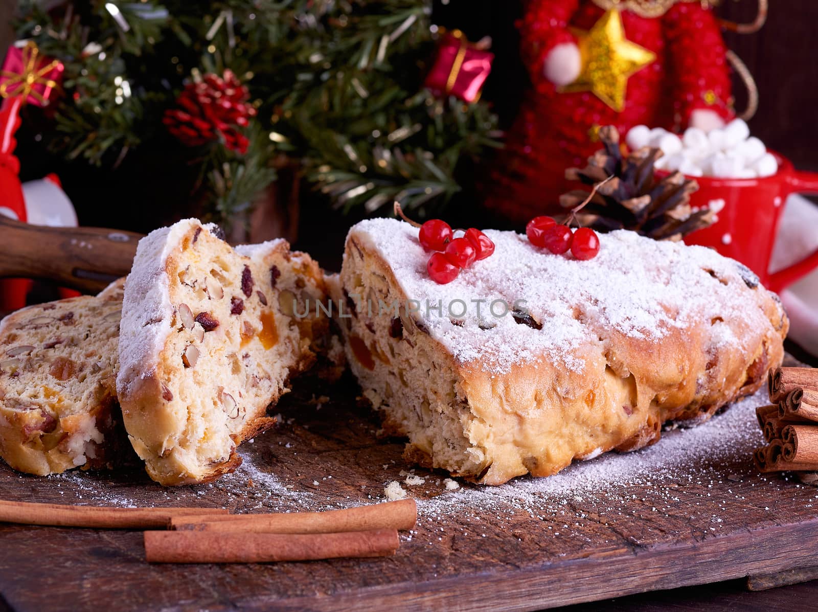 Stollen a traditional European cake with nuts and candied fruit, is dusted with icing sugar and cut into pieces on a brown wooden board