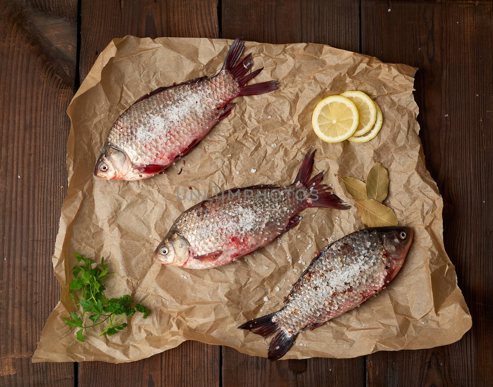 whole fresh crucian fish with scales on a crumpled brown piece of paper, top view