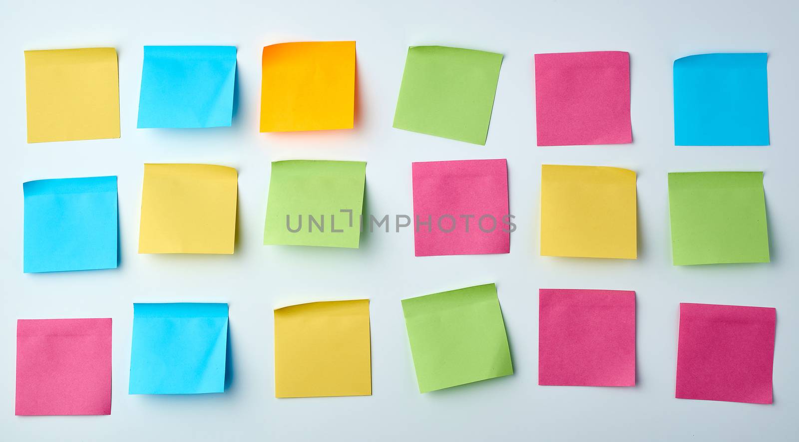 three rows of blank square paper multicolored stickers on a white wall, copy space