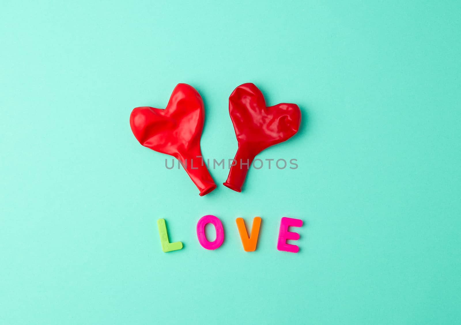 two red rubber balloons blow away in the shape of a heart on a green background
