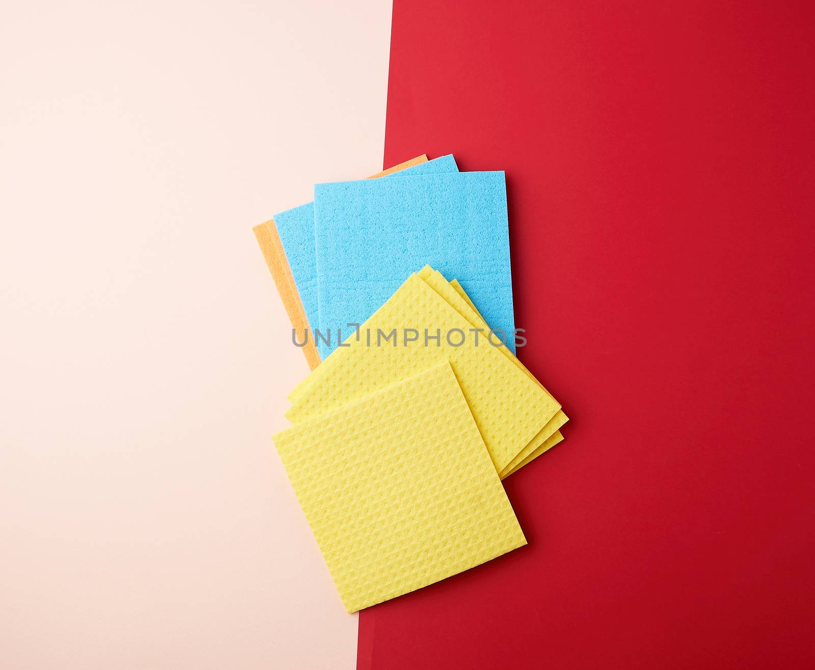multi-colored square dishwashing sponges on a red-beige background, top view, flat lay