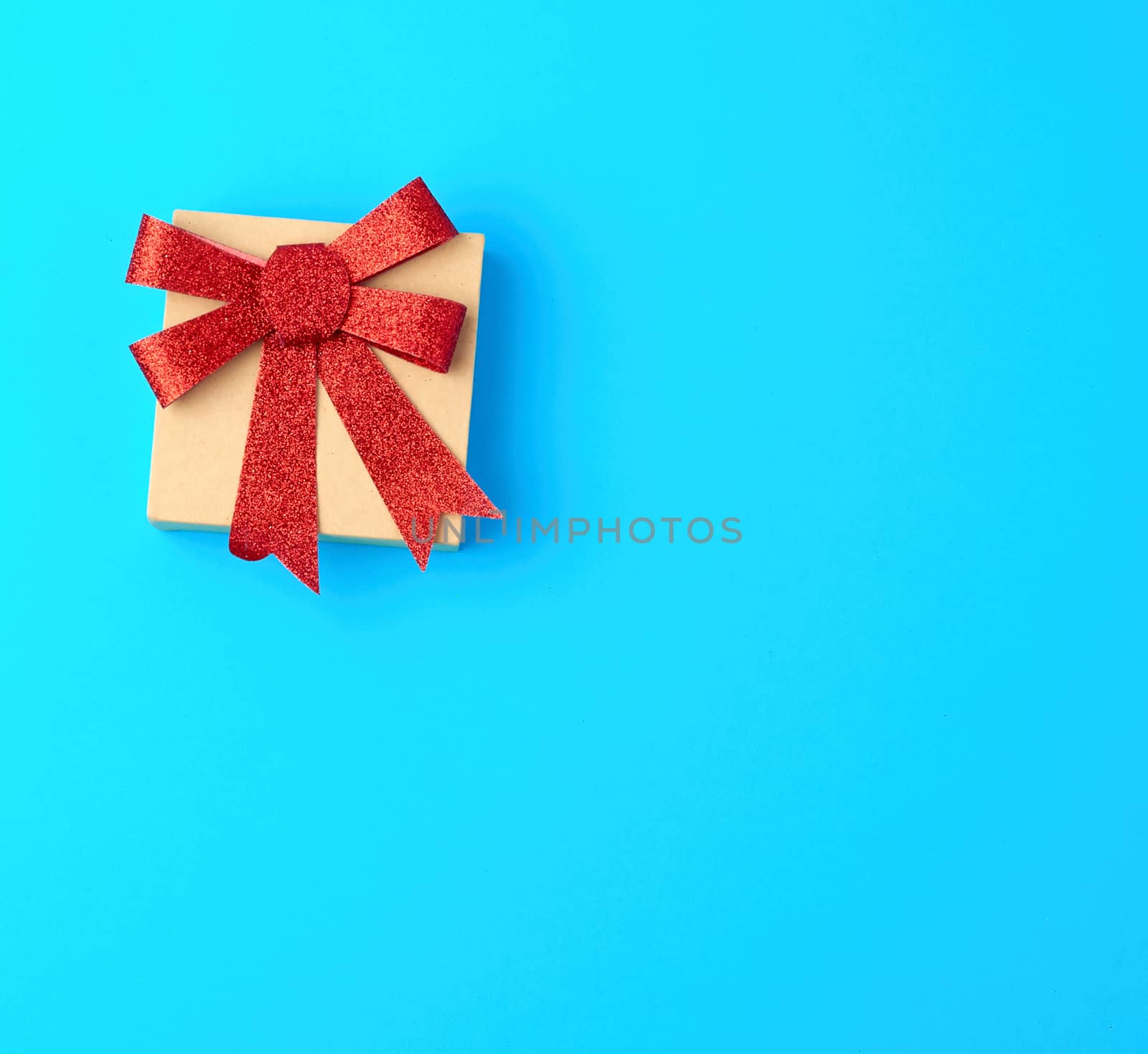 closed brown gift box with a red shiny bow on a blue background, top view, copy space