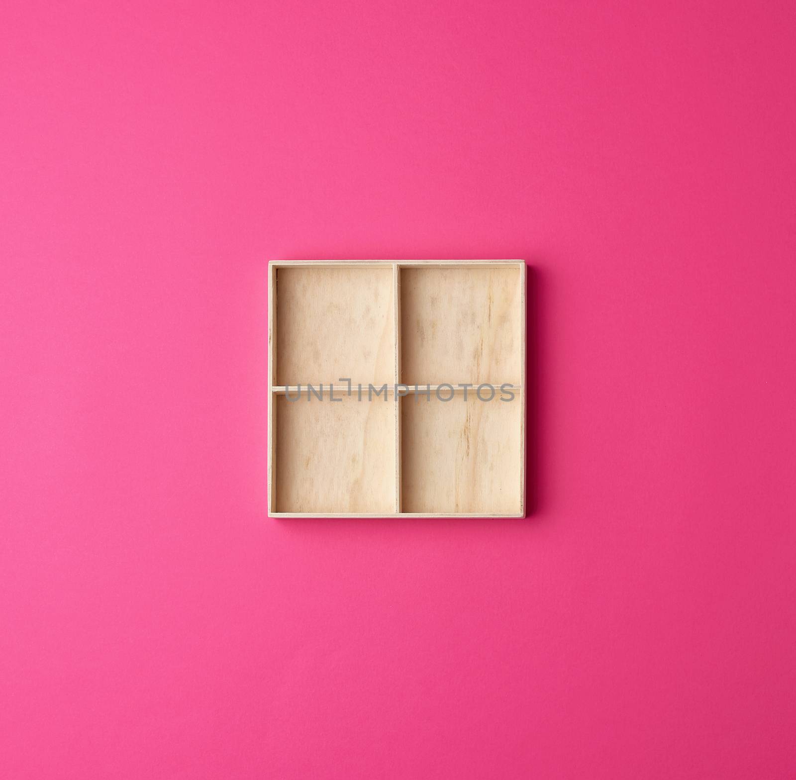 square wooden box divided into storage cells for small things on a pink background, top view