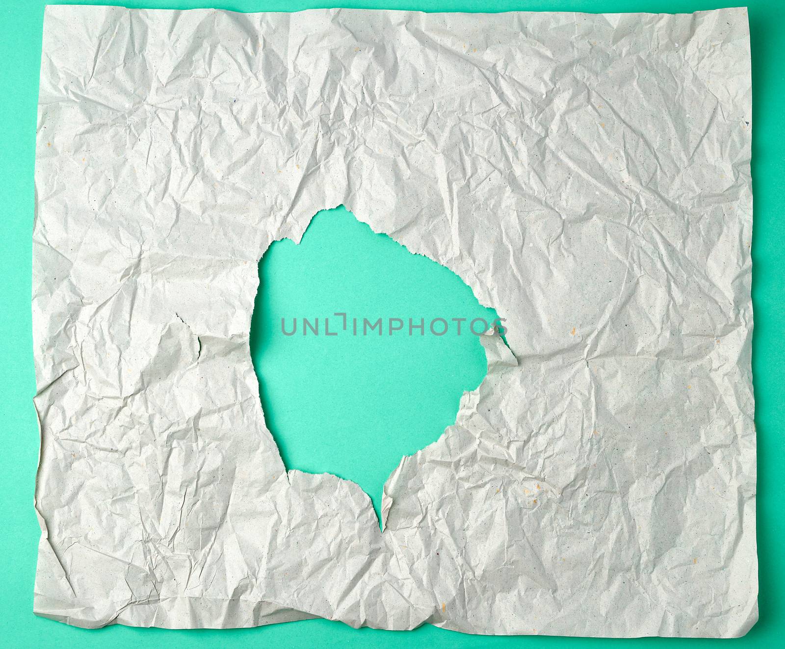 gray crumpled sheet of paper with a hole, green backing, abstract background