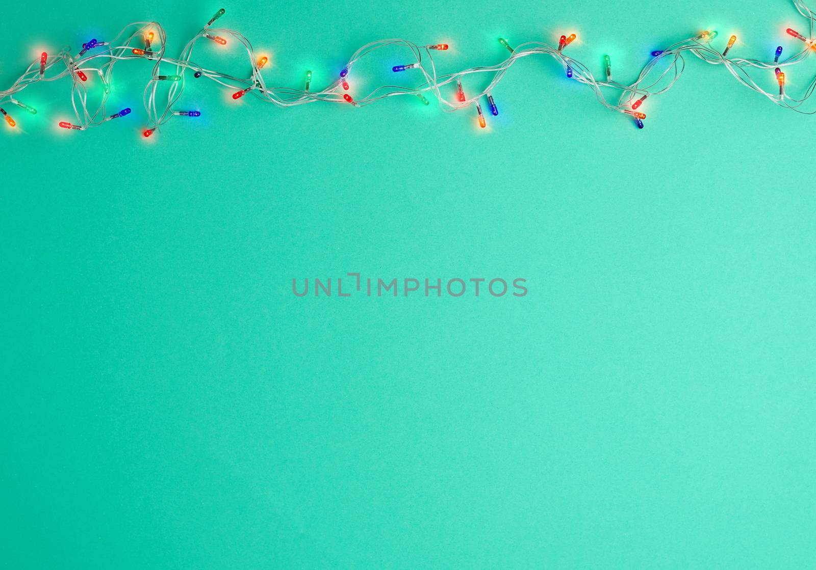 burning christmas garland on a white wire with colorful lights on a green background, copy space