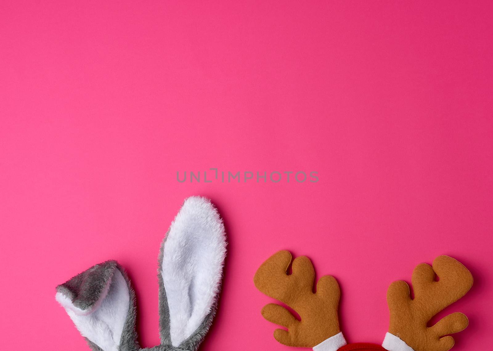 protruding ears of a rabbit mask and brown deer horns on a pink background, Christmas costumes, copy space