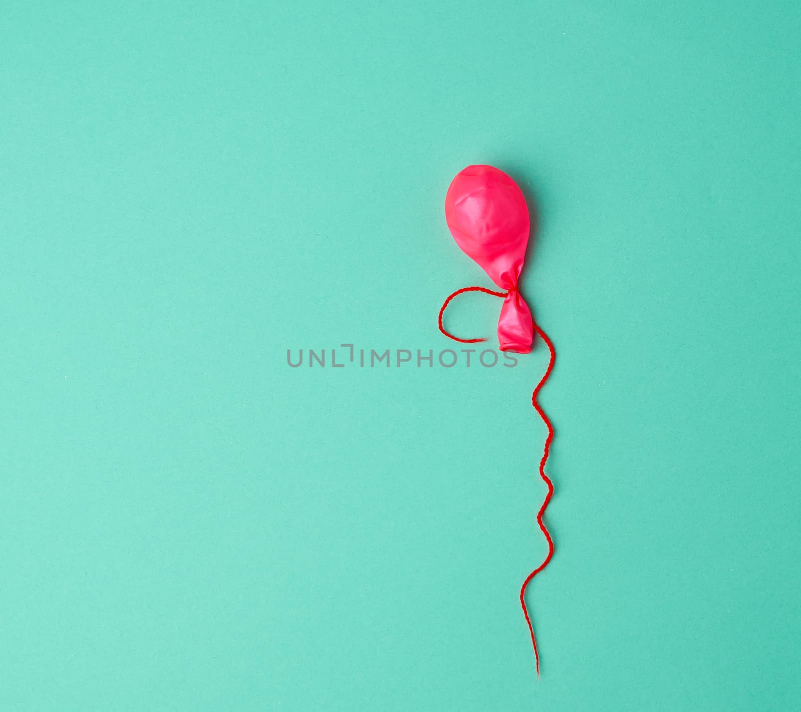 deflated rubber pink balloon and red rope on a green background, copy space