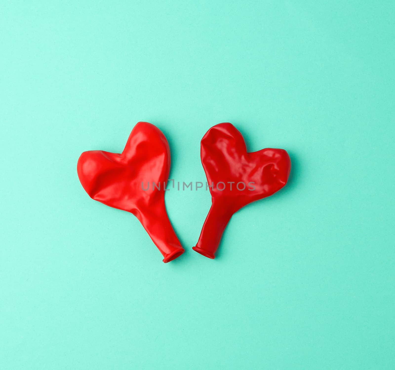 two red rubber balloons blow away in the shape of a heart on a green background