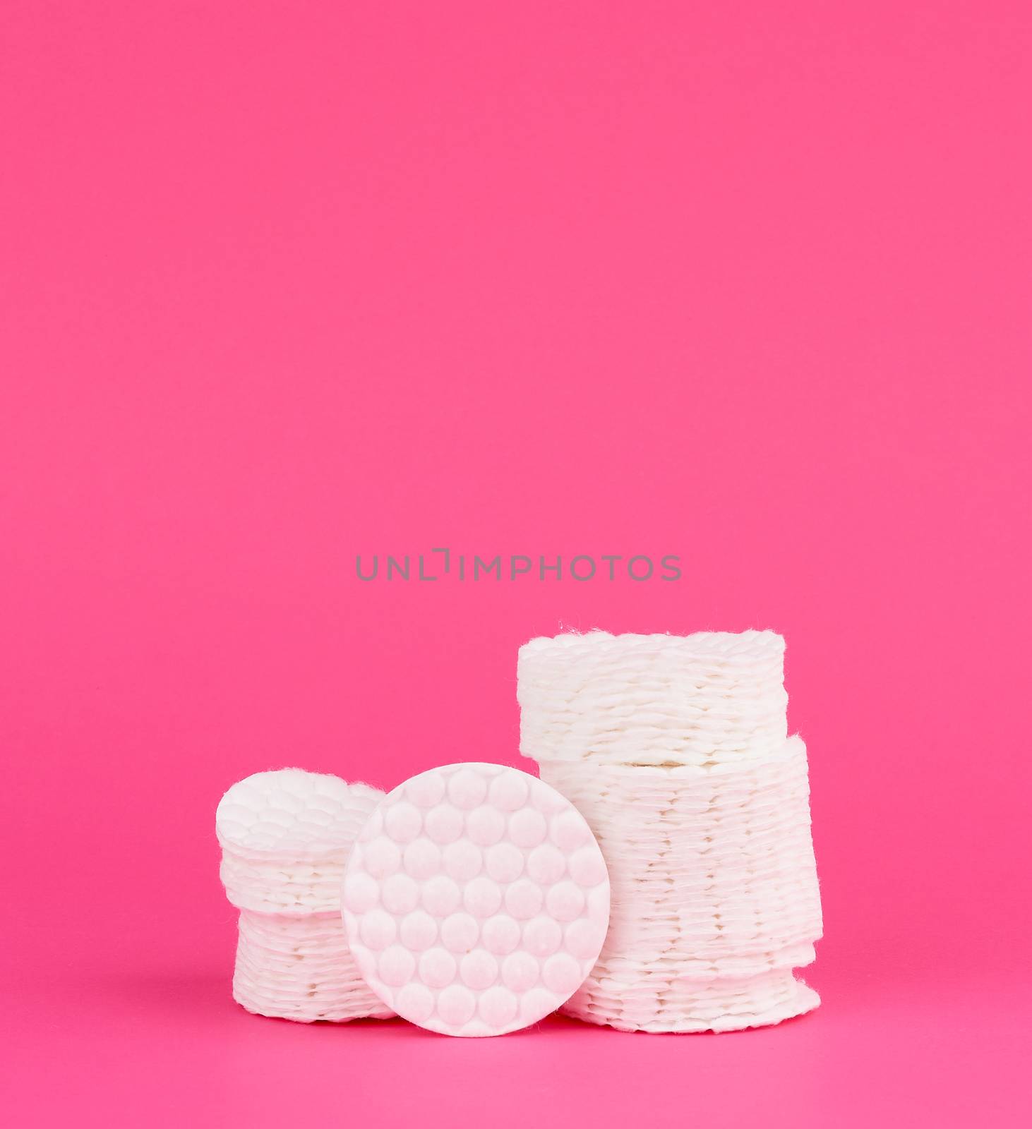 stack of white cotton round discs for cosmetic procedures on a pink background