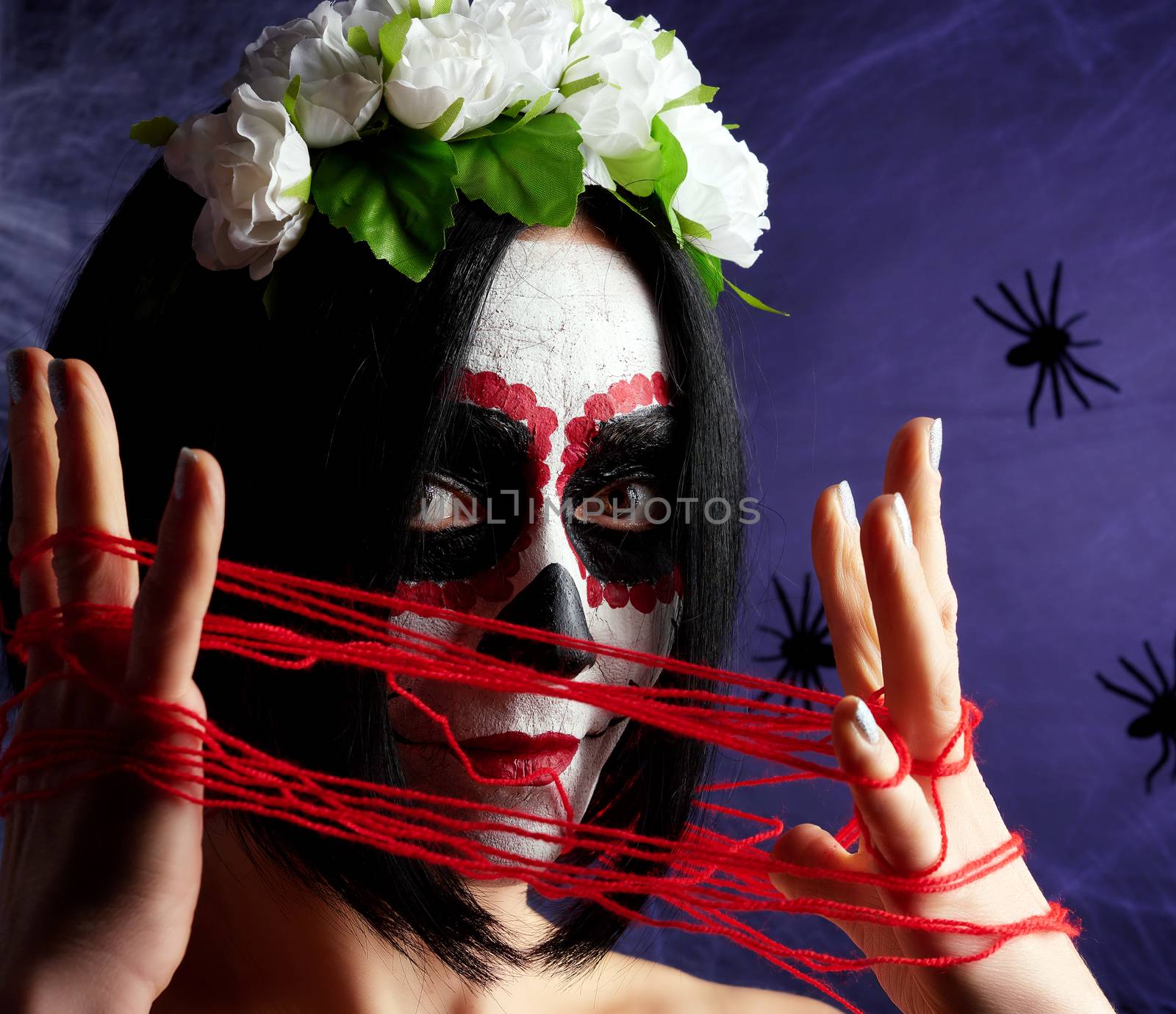 Young beautiful girl with traditional mexican death mask. Calavera Catrina. Sugar skull makeup. girl holds red woolen thread near the neck