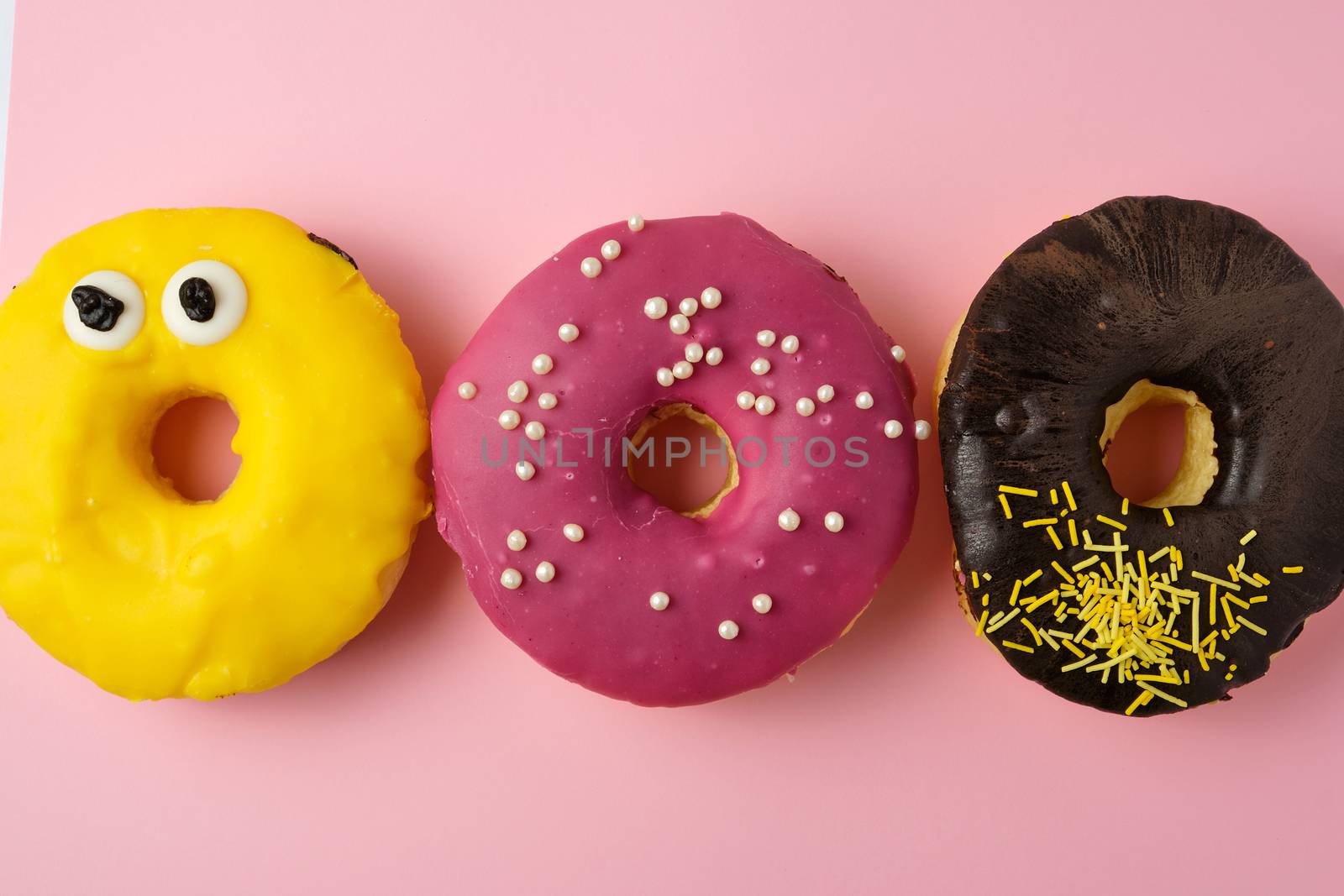 three round different sweet donuts with sprinkles on a yellow background, top view
