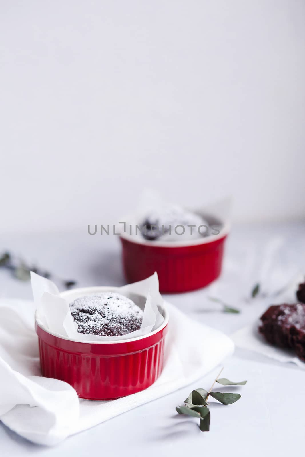 Chocolate muffins in red cups. Small glazed ceramic ramekin with brown cakes on a gray and white background. by Denys_N