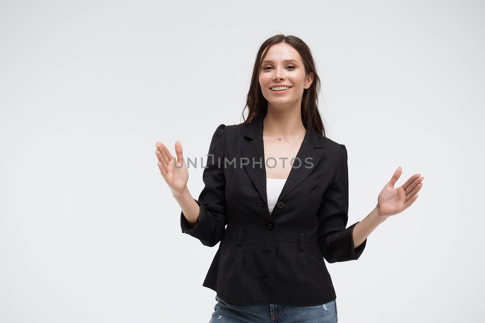 Positive optimistic young female in casual clothes gesturing and showing big size with hands while standing against white background
