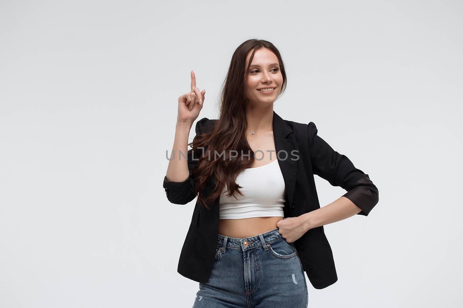 Smiling amazed young brunette in black turtleneck having idea and pointing forefinger up while standing against white background