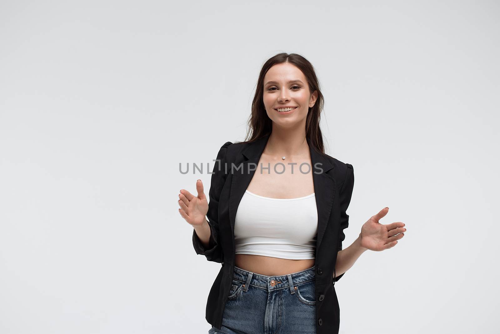 Positive optimistic young female in casual clothes gesturing and showing big size with hands while standing against white background