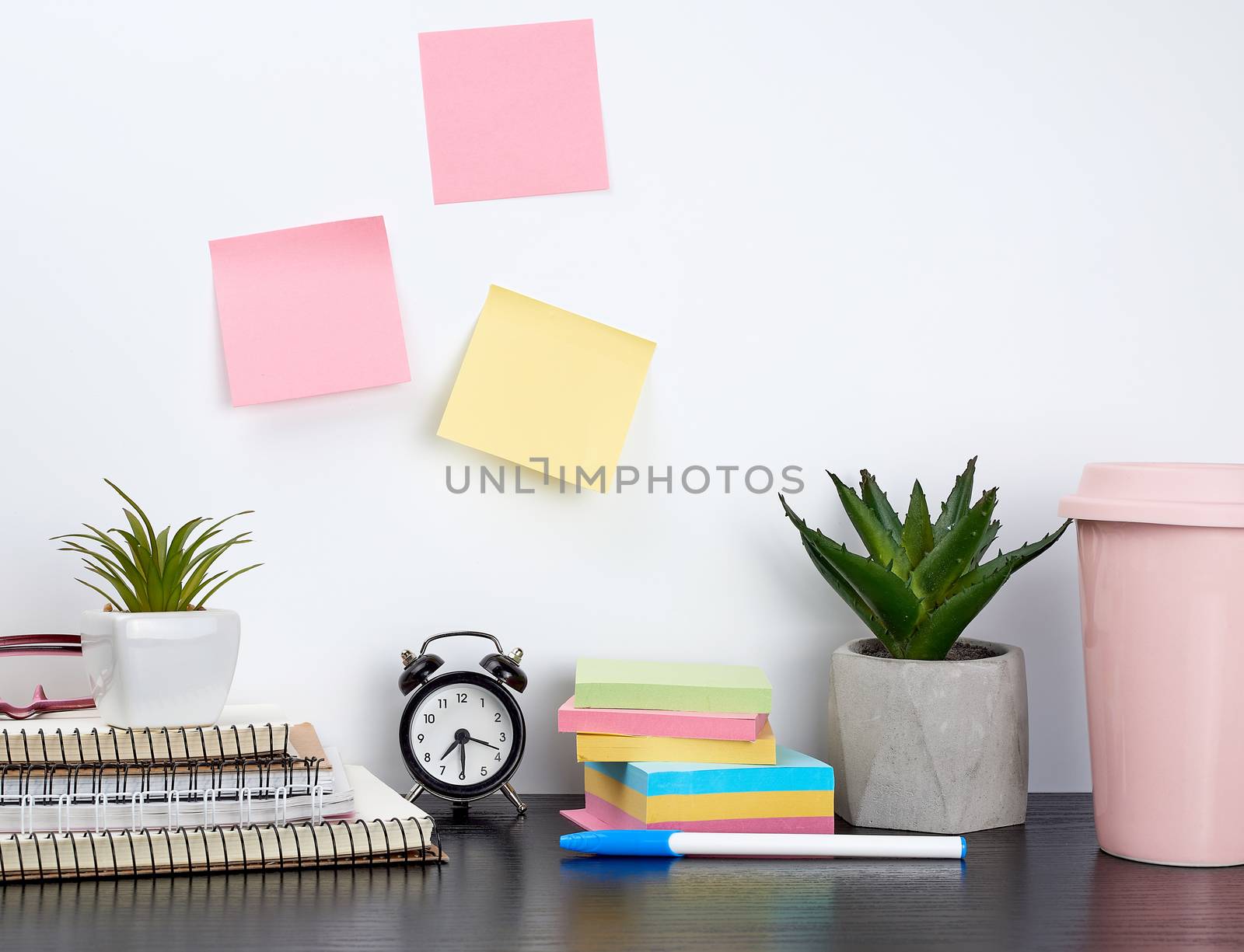 stack of spiral notebooks and colored stickers, next to a ceramic pot with a flower on a black table, white wall, Scandinavian-style minimalism
