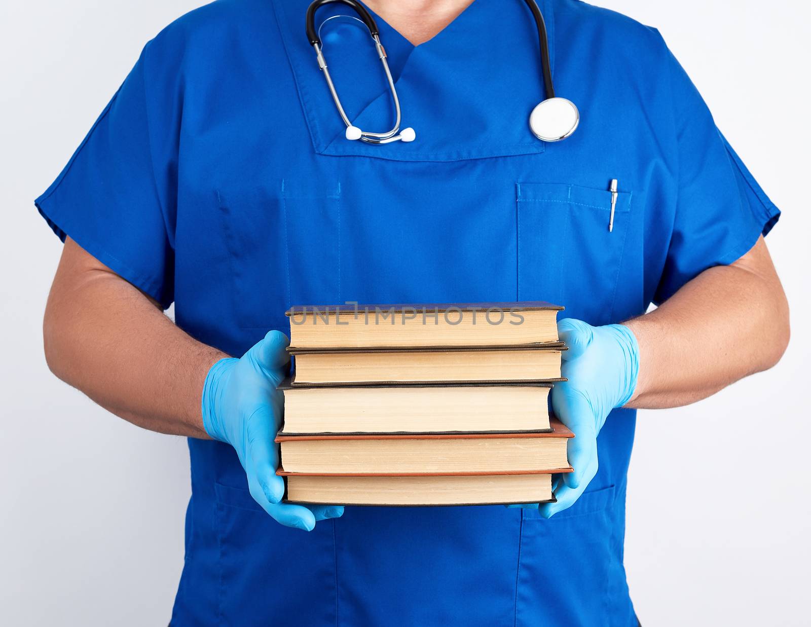 doctor in blue uniform and sterile latex gloves holds a stack of books in his hand against a white background, man stands in front