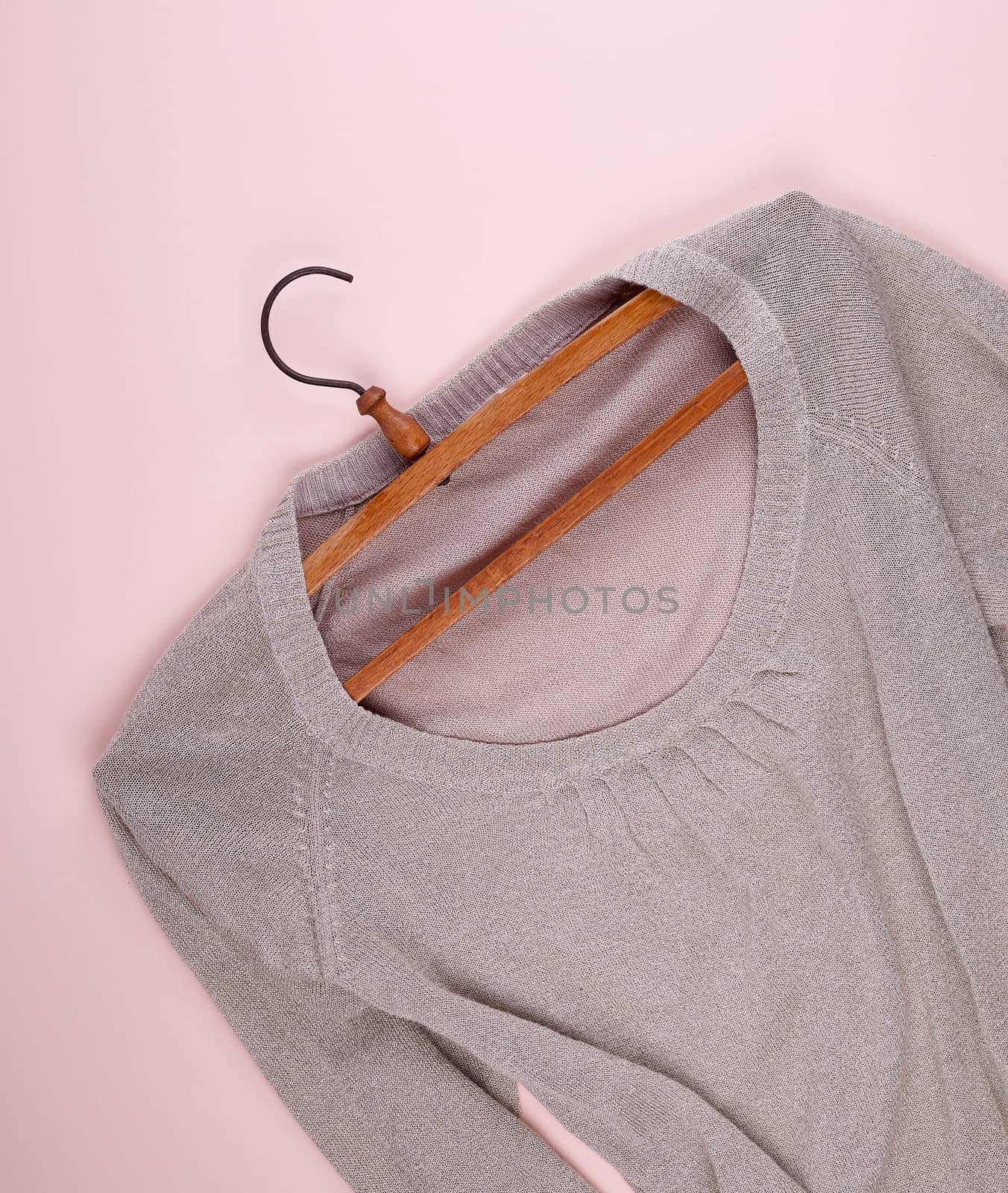 beige female sweater hanging on a vintage wooden hanger, beige background