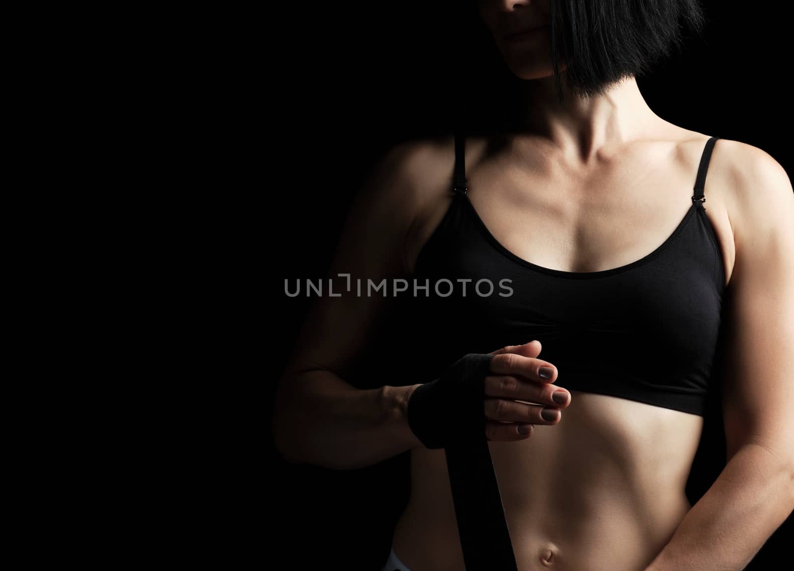 athletic girl with black hair rewinds her hand with a black elastic bandage before training, dark background