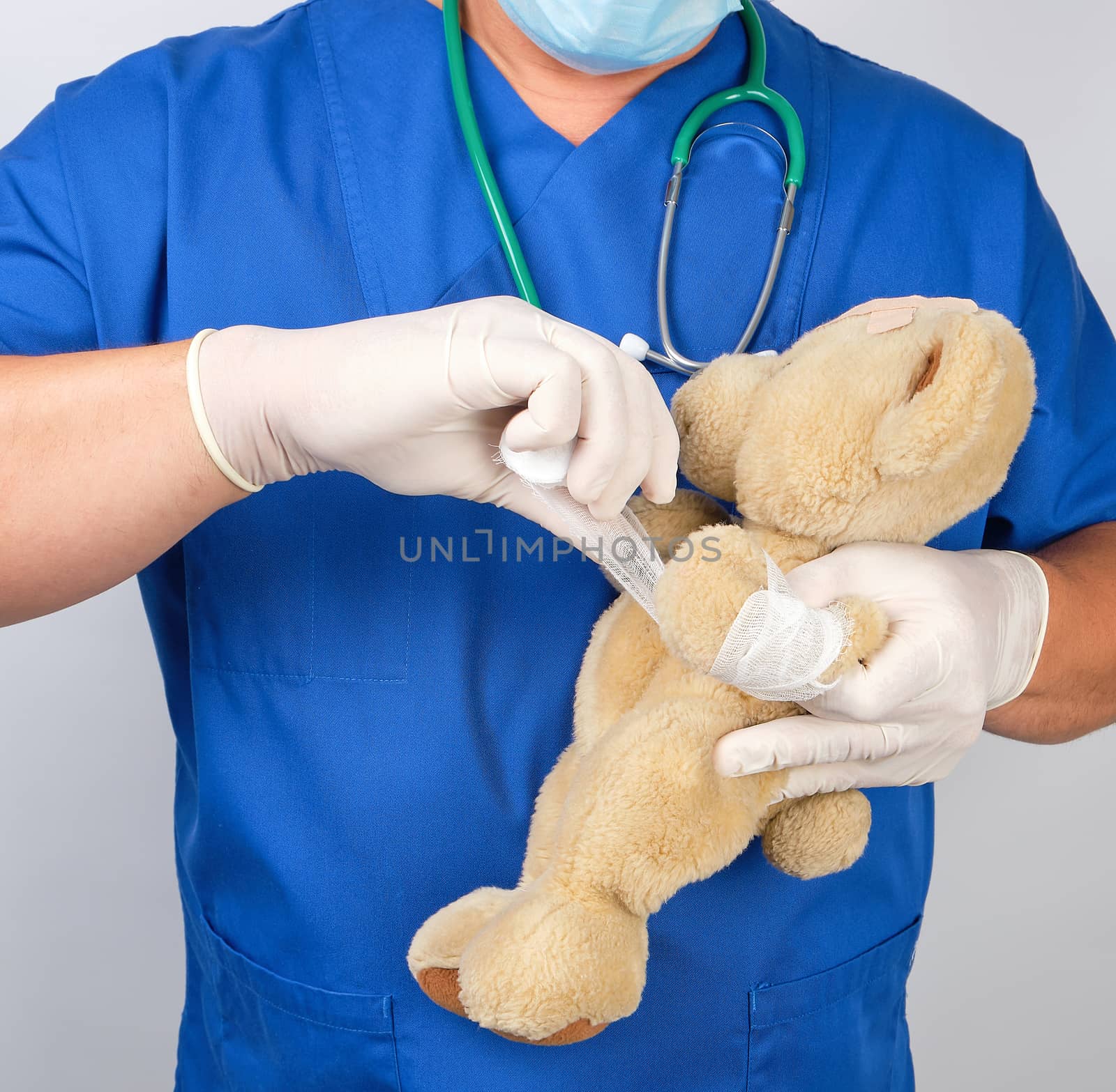 doctor in blue uniform bandages white medical bandage paw brown teddy bear, white background