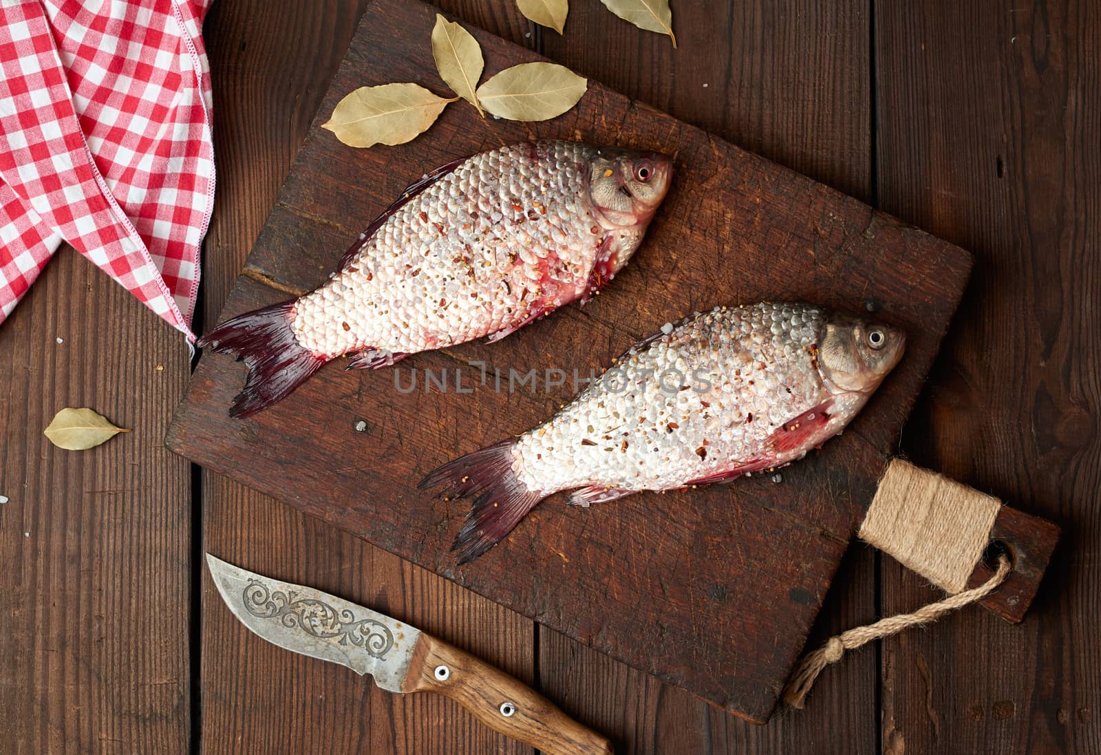 fresh crucian fish sprinkled with spices lies on a brown wooden cutting board, wooden table from boards, top view
