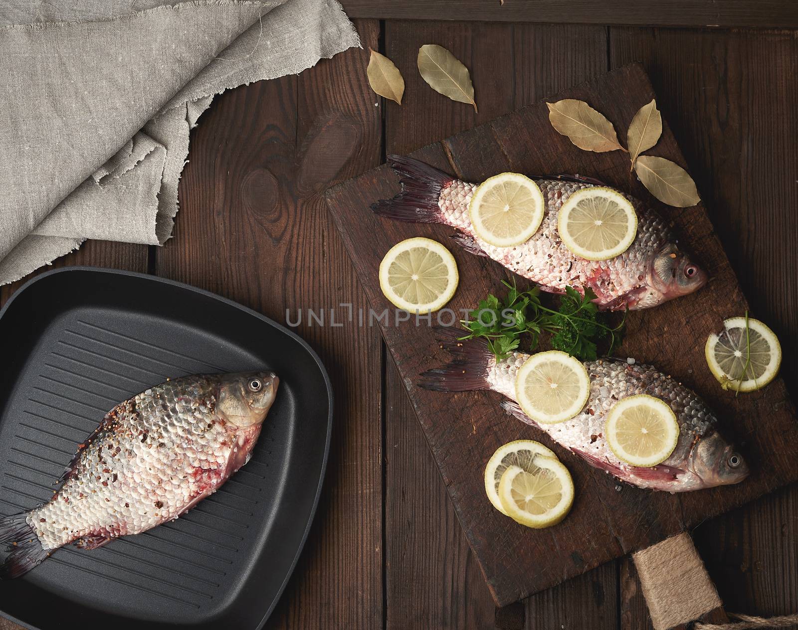 fresh crucian fish sprinkled with spices and lemon slices and lies on a brown wooden cutting board, wooden table from boards, top view