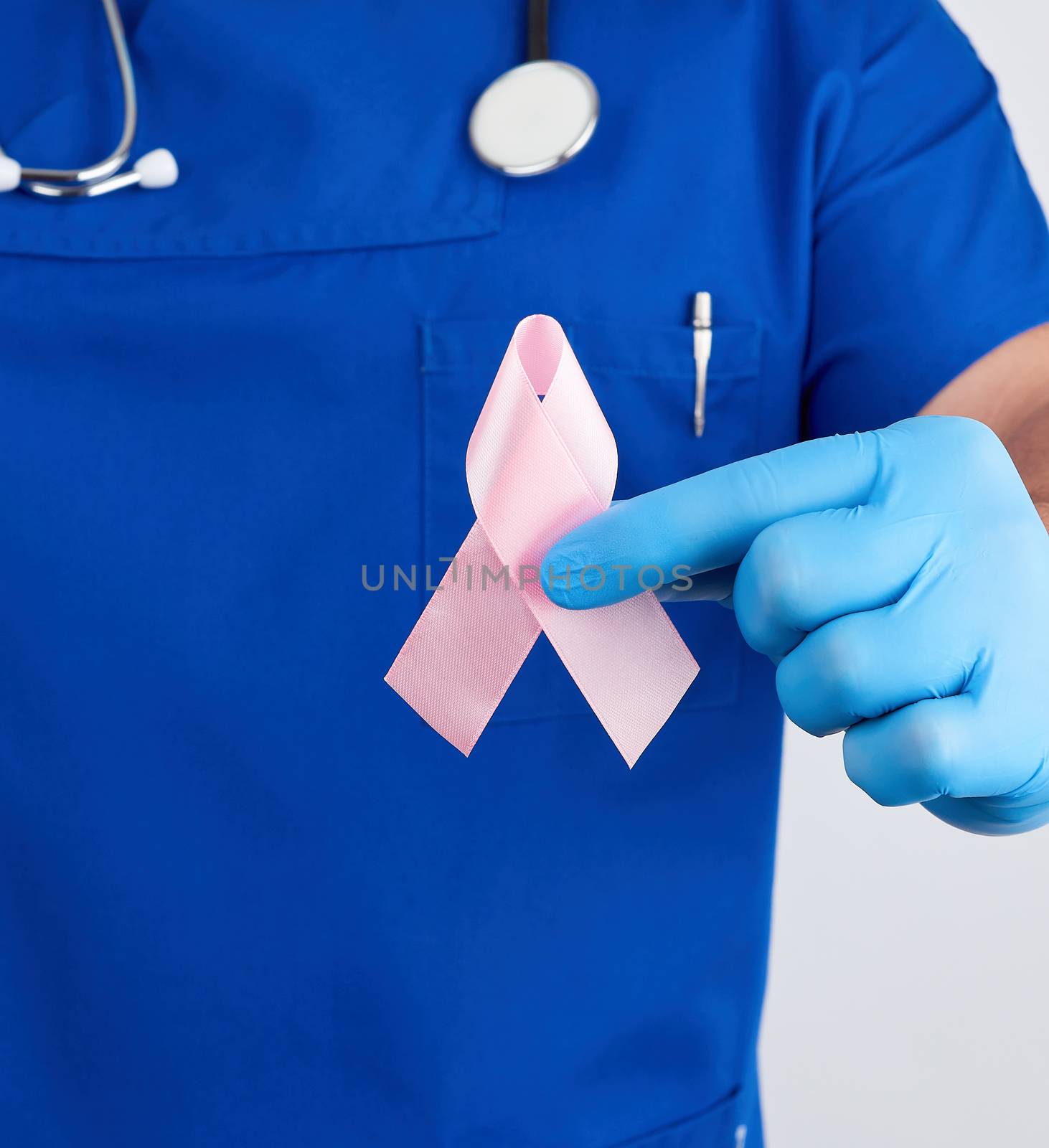 doctor in blue uniform and sterile latex gloves holds a pink ribbon a symbol of the fight against breast cancer in October every 20