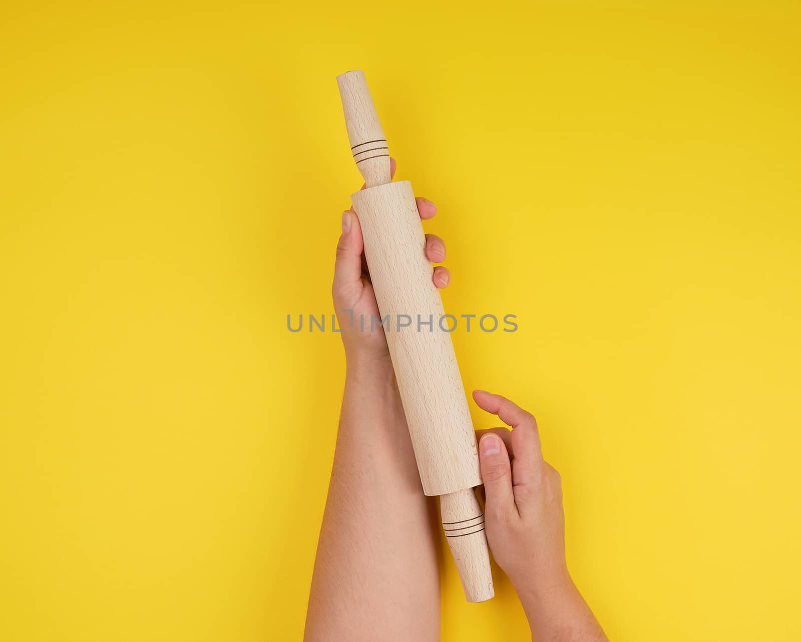 hand holding a wooden rolling pin on a yellow background, top view