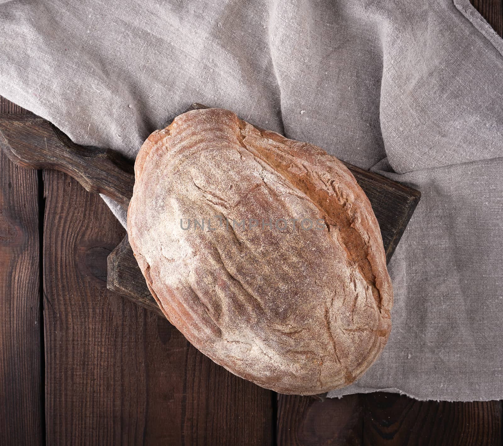 baked oval bread made from rye flour on a wooden cutting board, top view